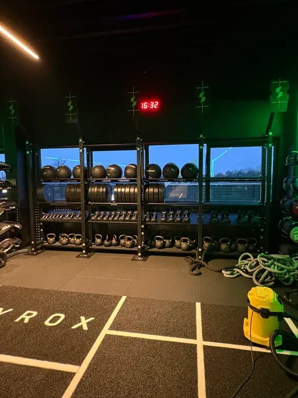 HYROX-zone met kettlebell-rack en battle ropes in donkere gym met groene LED